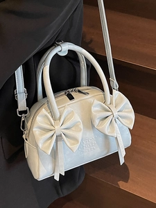 Sac Boston bleu clair verni avec nœuds, porté à l'épaule pour un style féminin et élégant