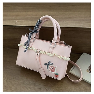 Detail of pink PU leather handbag with lace trim, strawberry charm and bowknot decoration
