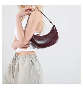 Détail du sac à main croissant bordeaux en cuir brillant porté à l'épaule de près