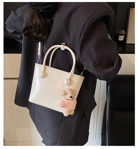 Detail of a creamy white bucket bag with a cute plush dog charm and brand lettering