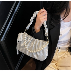 Detailed view of silver pleated dumpling bag with pearl strap and satin texture