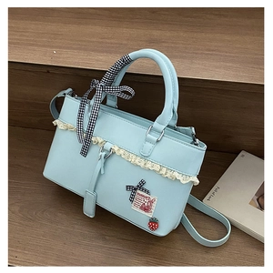 Detail of light blue crossbody bag with white lace trim and strawberry pendant charm