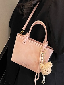 Pink bucket bag with plush charm and adjustable strap shown against a black blazer