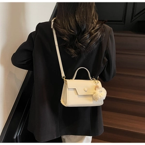 Dettaglio borsa squadrata color crema con ciondolo di peluche su blazer nero