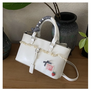 Detailed close-up of white leather handbag with lace trim, ribbon handle and strawberry charm