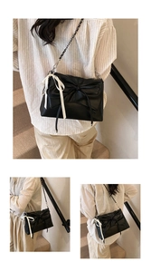 Detailed close-up of a black ballet-style pleated handbag with white ribbon and chain strap