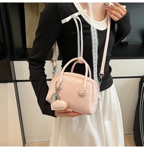 Detail view of pink glossy patent leather bowling bag with heart charm and shoulder strap