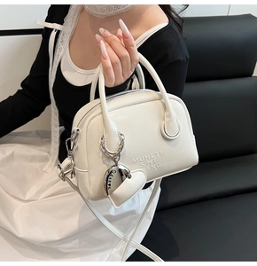 Detailed close-up of white glossy patent leather bowling bag with heart charm and shoulder strap