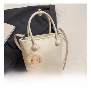 Detail view of cream bucket bag with decorative gold spheres and plush bear charm