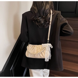 Close-up of beige ruched bag with pearl chain handle and delicate lace bow detail