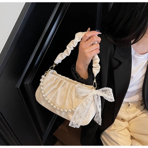 Detail of cream pleated handbag featuring pearl chain, lace bow, and scrunchie handle strap