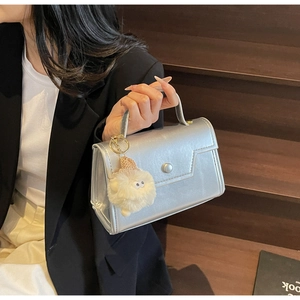 Dettaglio della borsa a patta argento con finitura metallizzata opaca e ciondolo peluche