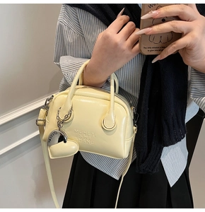 Close-up of cream yellow faux leather handbag with logo embossing and silver heart charm