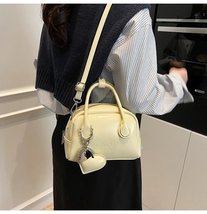 Detail view of cream oil-wax leather bowling bag with heart charm and shoulder strap