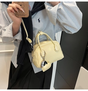 Detail of cream oil wax leather Boston bag with heart charm and crossbody strap worn by model