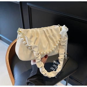 Close-up of pleated cream handbag featuring pearl chain strap and delicate lace ribbon