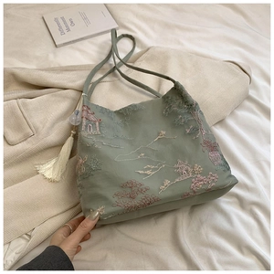 Broderie détaillée de paysages sur un sac cabas en soie verte avec pompon