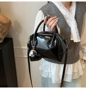 Detailed view of black patent leather bowling bag with heart charm shown on model