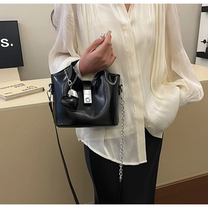 Détail d'un sac seau noir brillant avec fermoir argenté et pendentif en forme de cœur