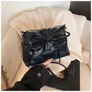 Detailed close-up of the black pleated underarm bag with a large ribbon bow and chain