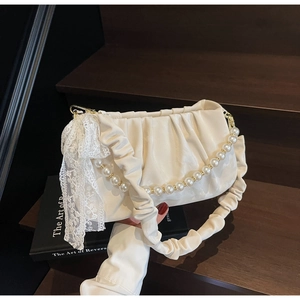 Close-up of a white pleated handbag featuring pearl chain and lace bow detail on wood