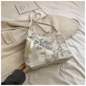 Détail de la broderie de pin sur un sac cabas en satin crème avec pompon décoratif