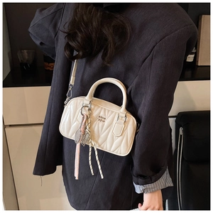 Close-up of quilted white crossbody bag with elegant wave texture and metal charm