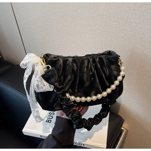 Detail of black pleated satin cloud bag with pearl strap and white lace bow decoration