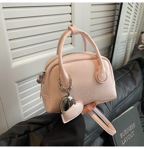 Detailed close-up of pink oil wax leather handbag featuring a heart charm and embossed logo