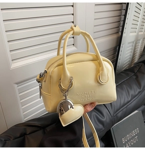 Detail view of cream yellow oil wax leather bowling bag with heart charm and strap