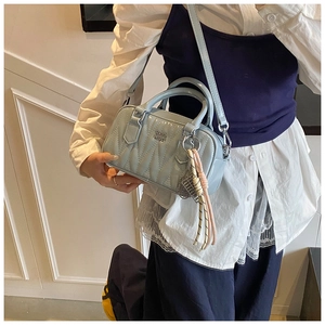 Detailed view of light blue quilted Boston bag with metal logo and woven pendant charm