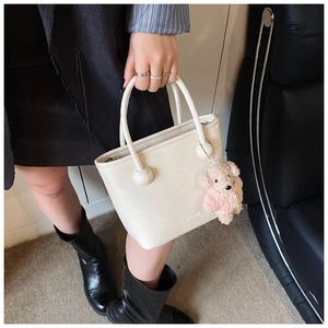 Detail of cream white leather bucket bag featuring metal sphere link and cute bear charm