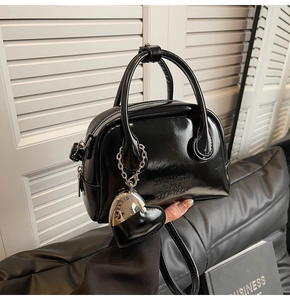 Close-up of black glossy bowling handbag with heart charm and logo embossing