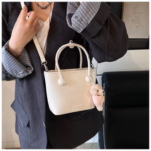Close-up of cream white bucket bag with cute teddy bear charm and adjustable strap
