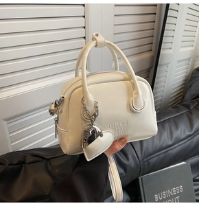 Detail of white oil wax leather handbag featuring heart-shaped metal charm and embossed text