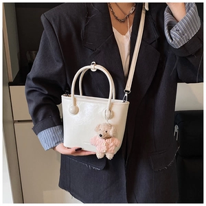 Detail showing white bucket bag with cylindrical handles and a cute plush bear charm