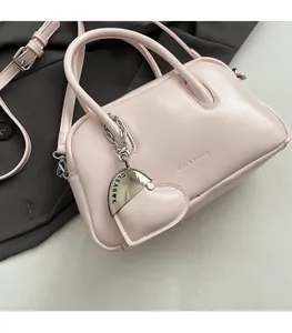 Close-up of light pink leather bag with silver heart pendant on dark grey suit fabric