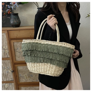Détail d'un sac cabas en paille crème orné de trois couches de franges et glands vert olive