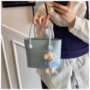 Detail view of light blue bucket bag with beaded handle and cute teddy bear charm