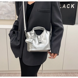 Détail du sac seau métallisé argenté avec pendentif cœur et bandoulière sur un blazer gris