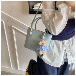 Light blue faux leather tote bag with cute plush bear charm in a stylish setting