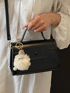 Borsa a mano minimalista nera in ecopelle con dettagli dorati e ciondolo in peluche