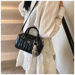 Close-up of black pleated quilted handbag featuring white letter print and stylish charms