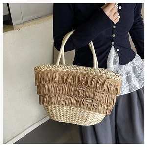 Détail d'un sac panier en paille d'été avec glands en raphia brun et anses tressées