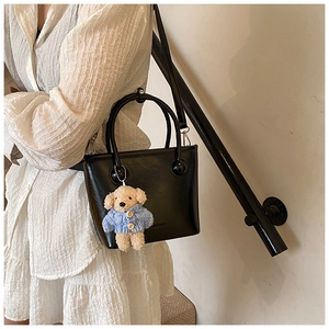 Detail of black glossy leather bucket bag with cute bear charm and metallic accents