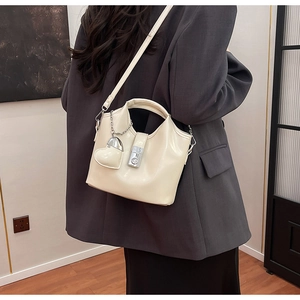 Détail d'un sac seau crème avec boucle métallique et pendentif cœur sur modèle