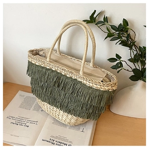 Détail d'un sac cabas en paille tressée avec pompons verts et fermeture éclair