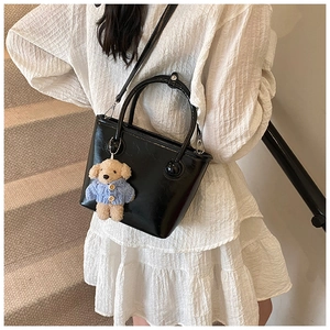 Detail of black glossy bucket bag with cute bear charm and spherical handle on white dress