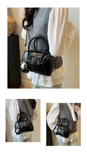 Detail of a black glossy patent leather pillow bag with heart pendant and shoulder strap