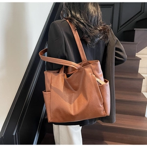 Detail of a brown leather tote bag with side pockets shown in a city commute setting